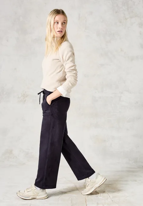 Frau mit beigefarbenem Pullover und dunkler Hose schaut seitlich und geht.
